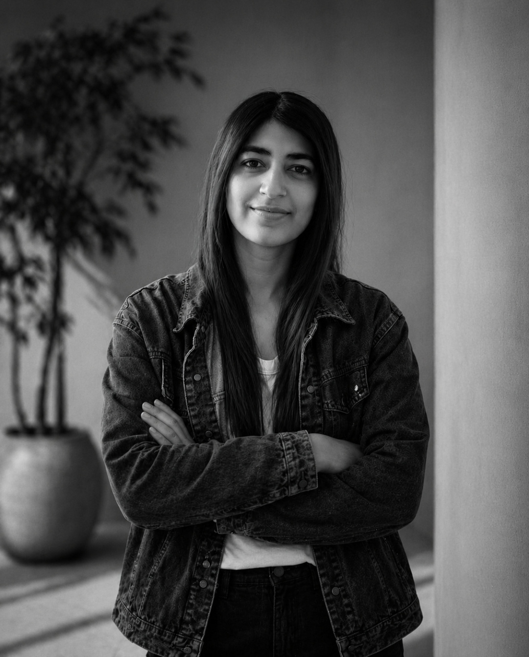Portrait of Dr. Tameer Siddiqui in a dark denim jacket, arms crossed, beside a potted plant